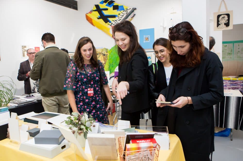 Visitors gather around a table to see items at the Boston Art Book Fair.
